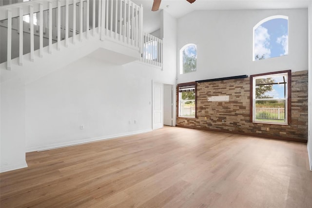 unfurnished living room with ceiling fan, brick wall, a high ceiling, wood finished floors, and baseboards