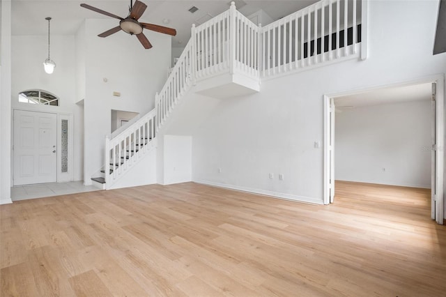 unfurnished living room with ceiling fan, a high ceiling, stairway, and wood finished floors