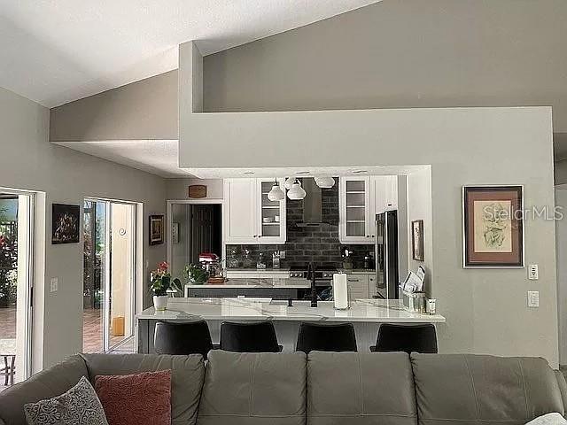 kitchen with white cabinets, vaulted ceiling, light countertops, tasteful backsplash, and stainless steel fridge