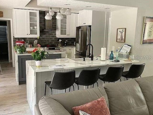 kitchen featuring light wood finished floors, open floor plan, a kitchen island with sink, white cabinets, and refrigerator with ice dispenser