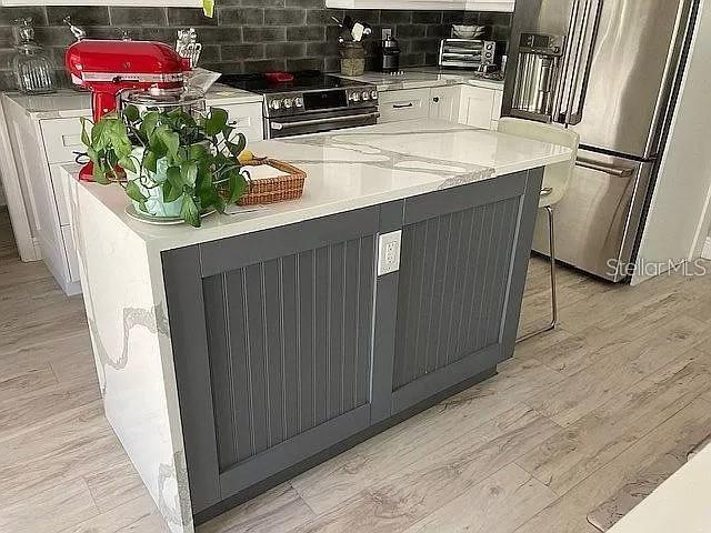 kitchen with stainless steel appliances, white cabinets, light countertops, light wood finished floors, and tasteful backsplash