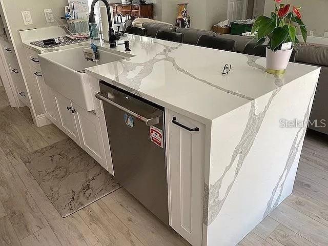 kitchen with light stone counters, light wood-type flooring, stainless steel dishwasher, white cabinetry, and a sink