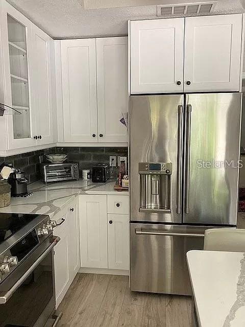 kitchen with stainless steel appliances, visible vents, glass insert cabinets, white cabinetry, and light wood-type flooring