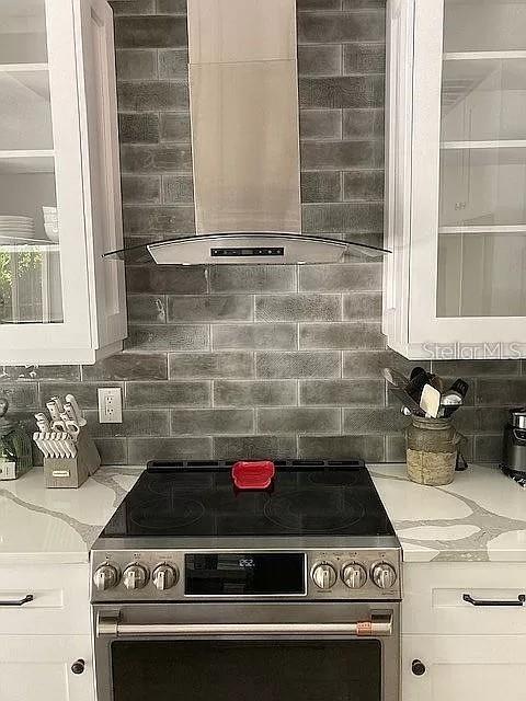 kitchen with white cabinetry, electric stove, backsplash, light stone countertops, and wall chimney exhaust hood