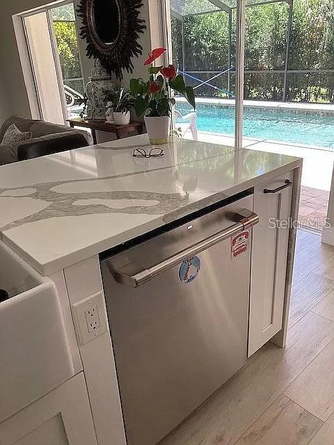 kitchen with light wood-style flooring, light stone counters, white cabinets, and dishwasher