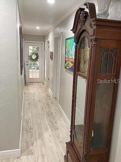 hallway featuring light wood-style floors, baseboards, ornamental molding, and a textured wall