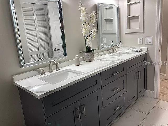 full bath with marble finish floor, a sink, baseboards, and double vanity