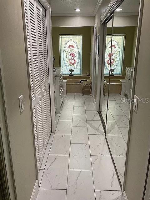 hall with a textured ceiling, marble finish floor, and ornamental molding