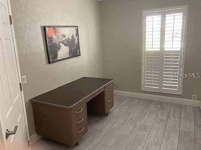 unfurnished office featuring a textured wall, light wood-style flooring, and baseboards