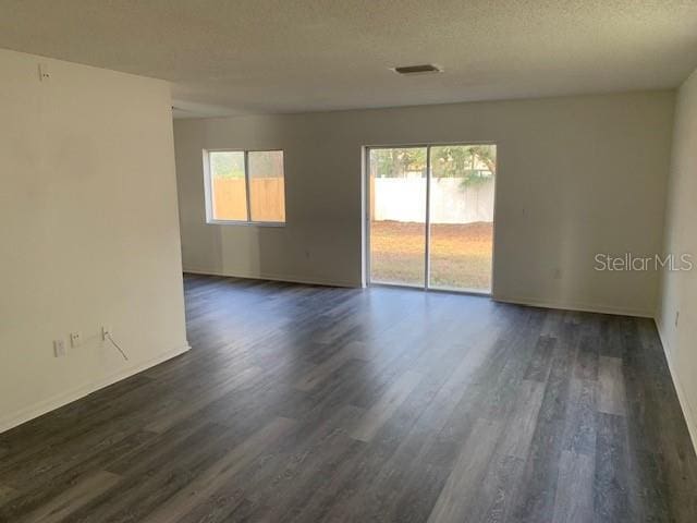 unfurnished room featuring dark wood-style floors, a textured ceiling, visible vents, and a wealth of natural light