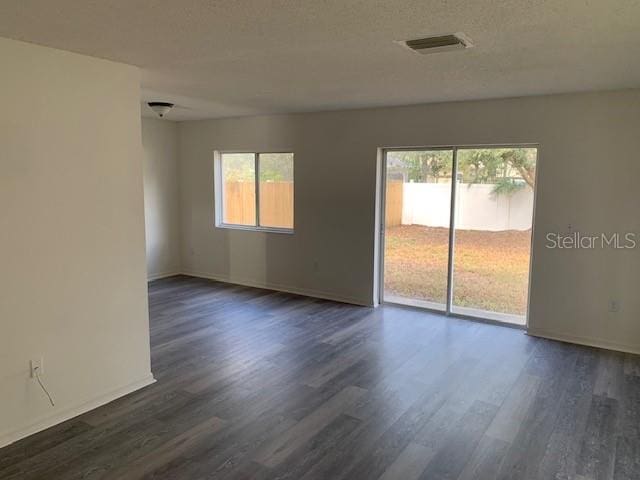 spare room featuring dark wood-style floors, a wealth of natural light, a textured ceiling, and visible vents