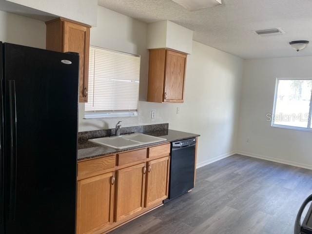 kitchen with dark wood-style floors, dark countertops, visible vents, a sink, and black appliances