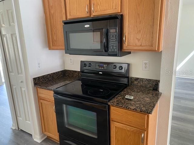 kitchen featuring dark stone counters, black appliances, and wood finished floors