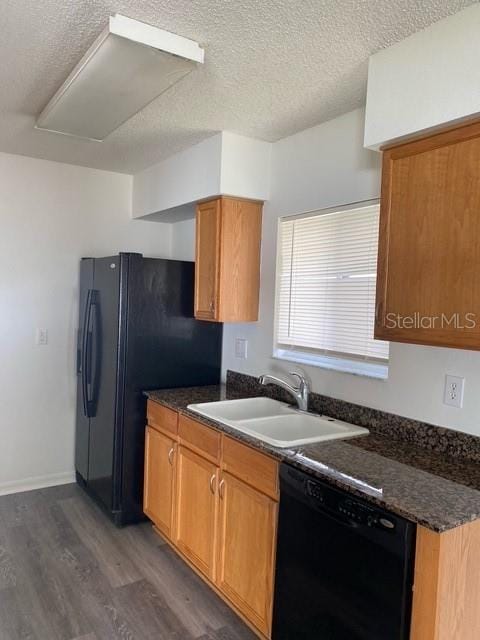 kitchen with dark countertops, black appliances, dark wood-type flooring, and a sink