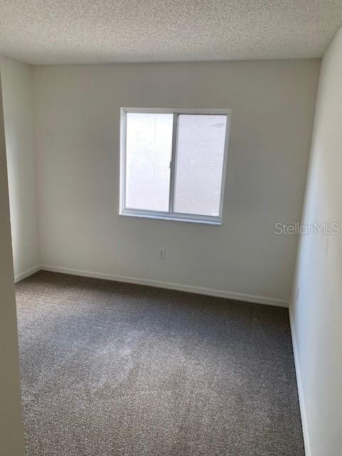 carpeted spare room with a textured ceiling and baseboards