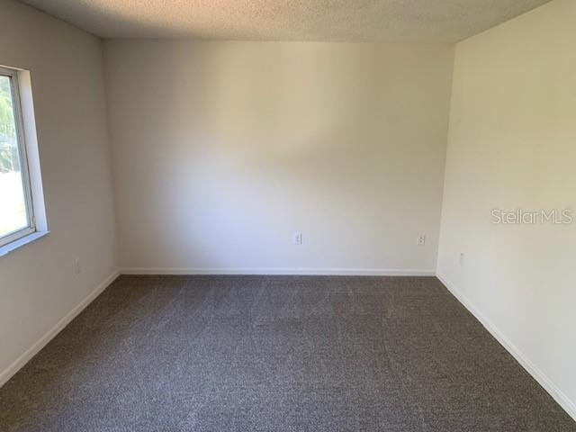 unfurnished room with baseboards, dark carpet, and a textured ceiling