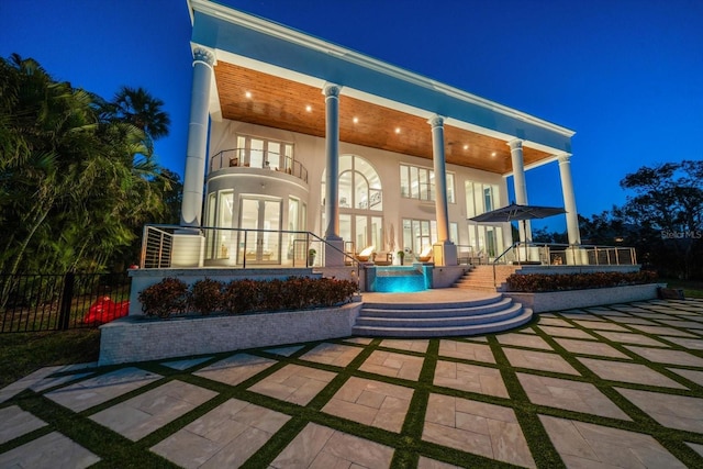 back of house at night with a patio, french doors, a balcony, and stucco siding