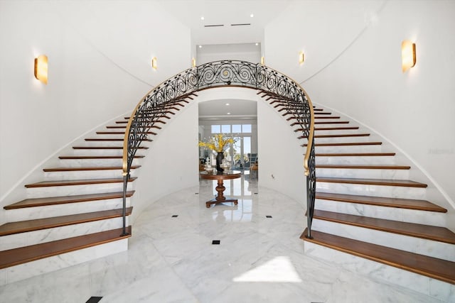 stairway featuring arched walkways, marble finish floor, and a towering ceiling