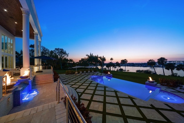 view of pool featuring a water view, a patio area, an infinity pool, and a yard