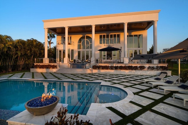 back of property with a fenced in pool, a patio, a fire pit, and a balcony