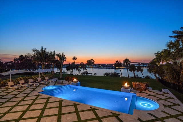 pool at dusk with a lawn, a patio area, a pool with connected hot tub, and a water view