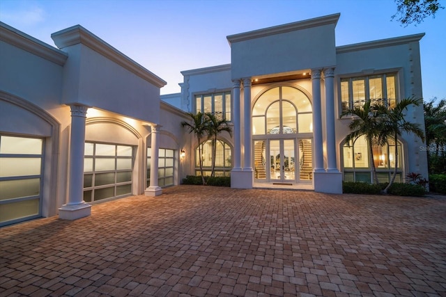 back of property at dusk with french doors, decorative driveway, and stucco siding