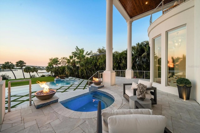 pool at dusk with an outdoor fire pit, an outdoor pool, a water view, and a patio