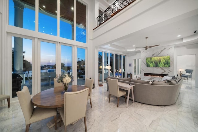 dining area featuring a towering ceiling, ceiling fan, marble finish floor, a fireplace, and recessed lighting