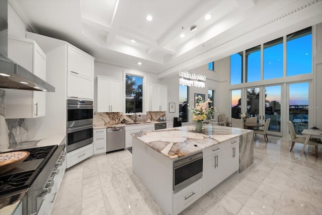 kitchen with coffered ceiling, wall chimney exhaust hood, a kitchen island, appliances with stainless steel finishes, and marble finish floor