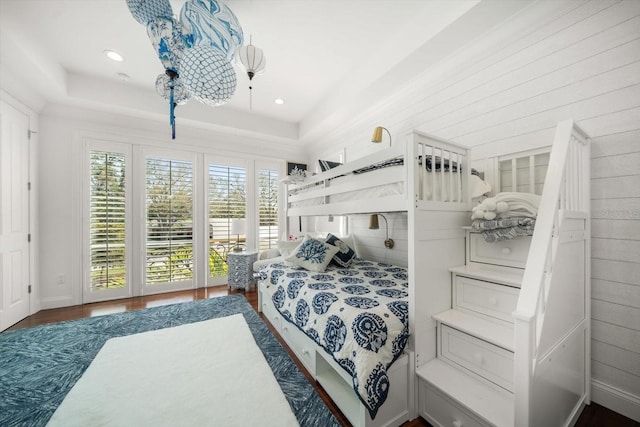 bedroom with wood walls, a tray ceiling, wood finished floors, and recessed lighting