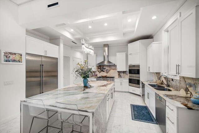 kitchen with a sink, wall chimney range hood, a large island, appliances with stainless steel finishes, and light stone countertops