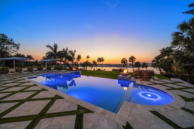 pool at dusk with an outdoor pool, a patio area, a jacuzzi, a water view, and a yard