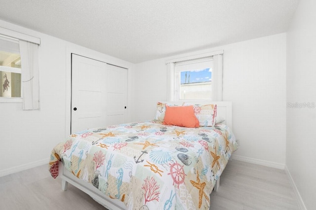 bedroom with wood finished floors, baseboards, a closet, and a textured ceiling