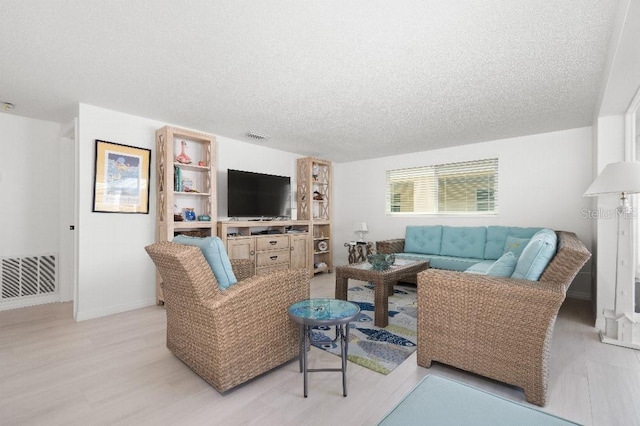 living area featuring visible vents, baseboards, a textured ceiling, and light wood-style flooring