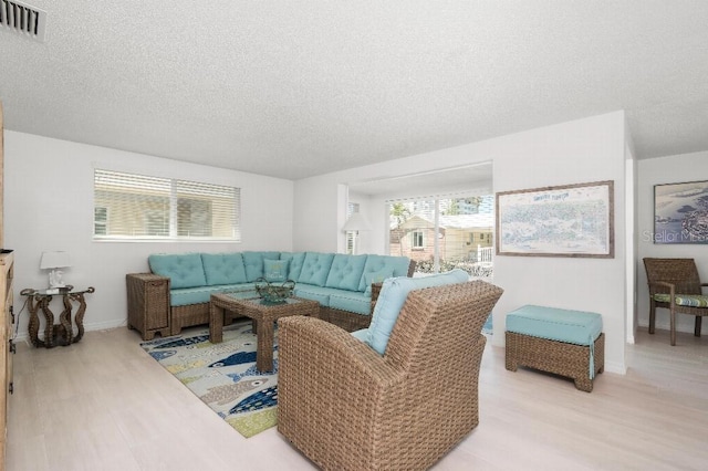 living room with baseboards, visible vents, light wood finished floors, and a textured ceiling