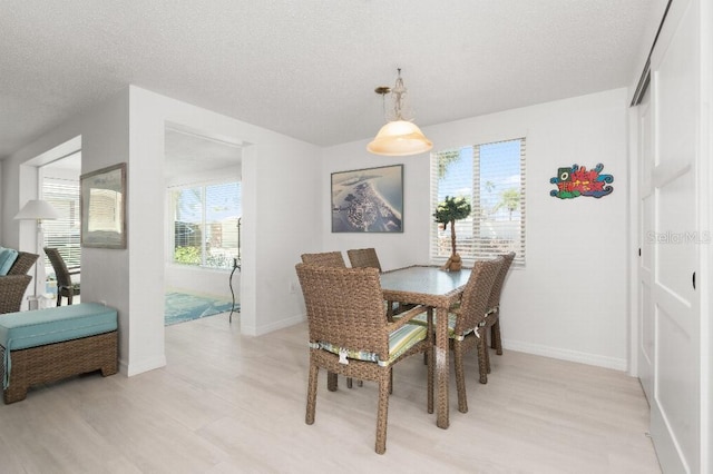 dining room with light wood-style flooring, a textured ceiling, and baseboards