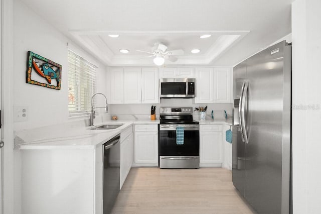 kitchen with a sink, light countertops, white cabinets, appliances with stainless steel finishes, and a raised ceiling