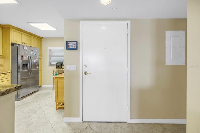 kitchen with light tile patterned floors, stone counters, baseboards, stainless steel refrigerator with ice dispenser, and electric panel