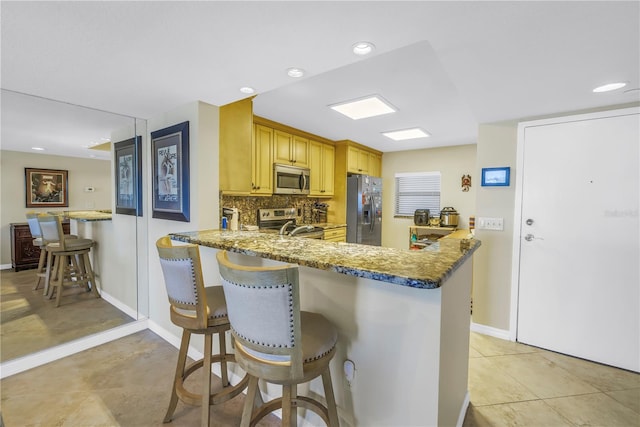 kitchen featuring a peninsula, appliances with stainless steel finishes, stone counters, and tasteful backsplash