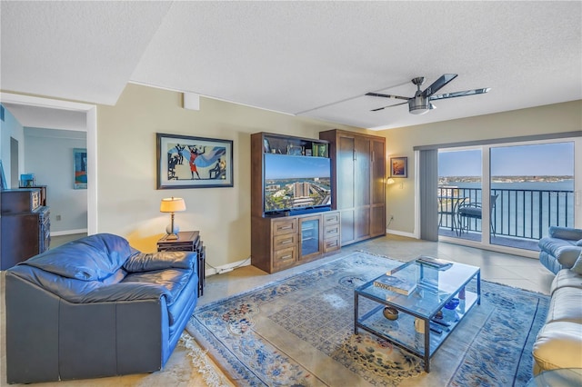 living area featuring a ceiling fan, light tile patterned flooring, a textured ceiling, and baseboards