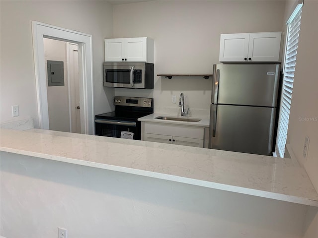 kitchen with stainless steel appliances, electric panel, a sink, and light stone countertops