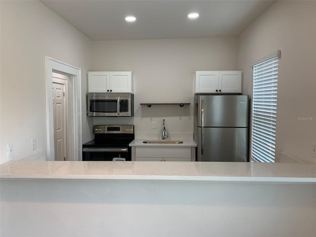 kitchen with recessed lighting, a sink, white cabinets, appliances with stainless steel finishes, and light stone countertops