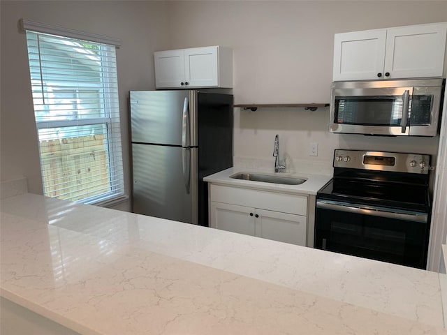 kitchen featuring stainless steel appliances, a sink, white cabinetry, and light stone countertops