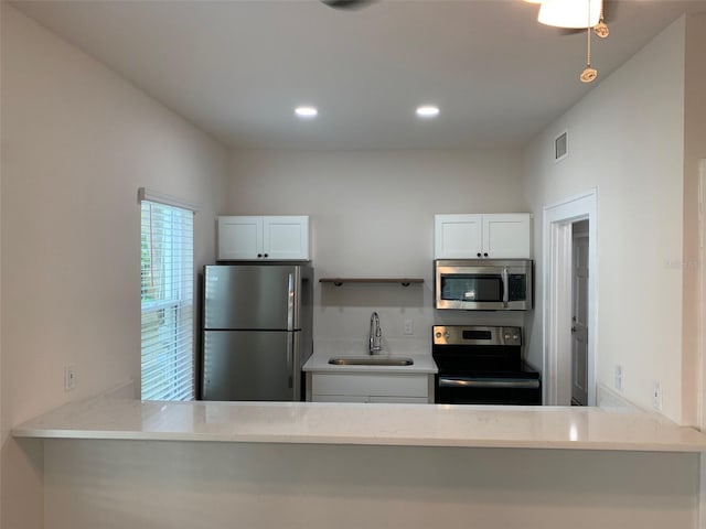 kitchen featuring a peninsula, a sink, visible vents, white cabinetry, and appliances with stainless steel finishes