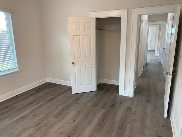 unfurnished bedroom with dark wood-style floors, baseboards, and a closet