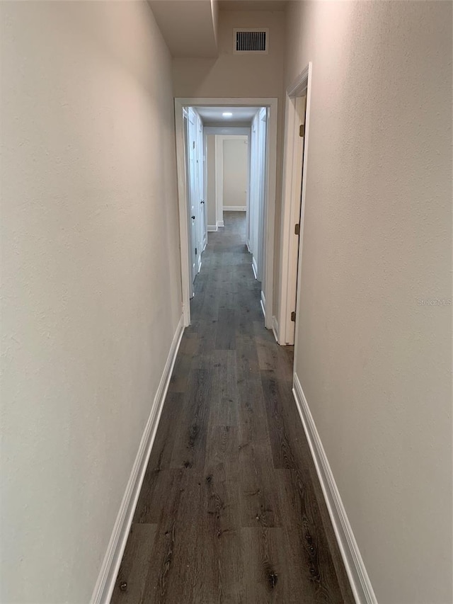 corridor featuring dark wood-style floors, visible vents, and baseboards