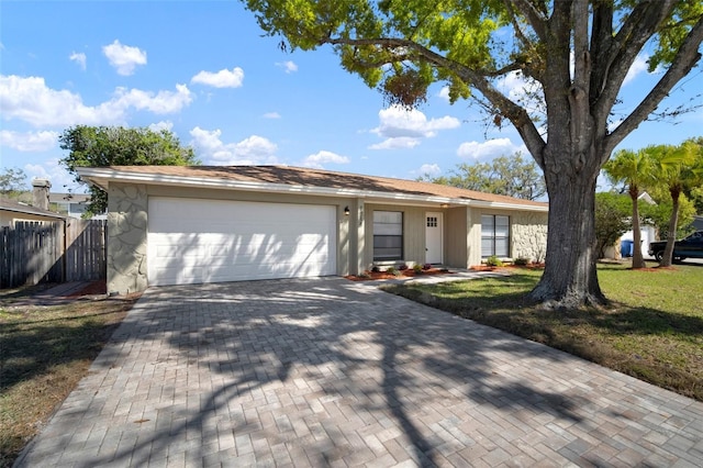 single story home with an attached garage, fence, decorative driveway, and a front yard