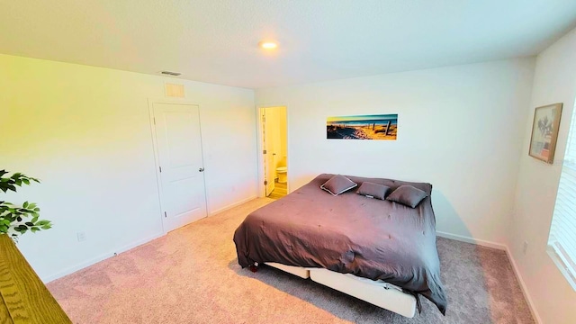 carpeted bedroom with ensuite bath, visible vents, and baseboards