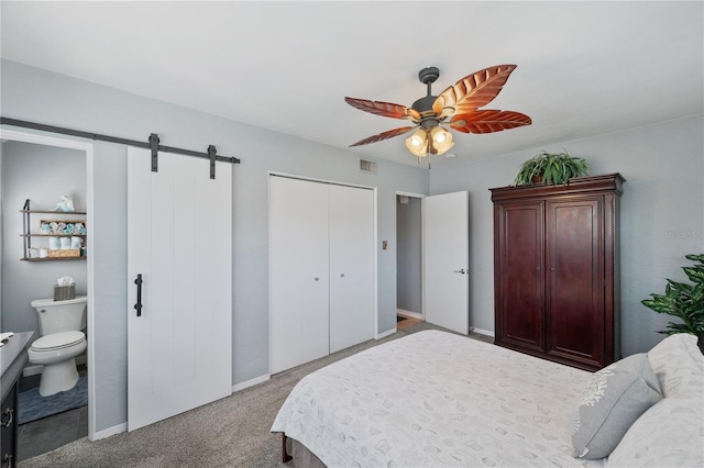 carpeted bedroom with a barn door, visible vents, baseboards, a closet, and ensuite bath