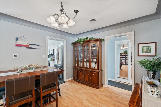 dining room featuring a chandelier, light wood finished floors, visible vents, and baseboards